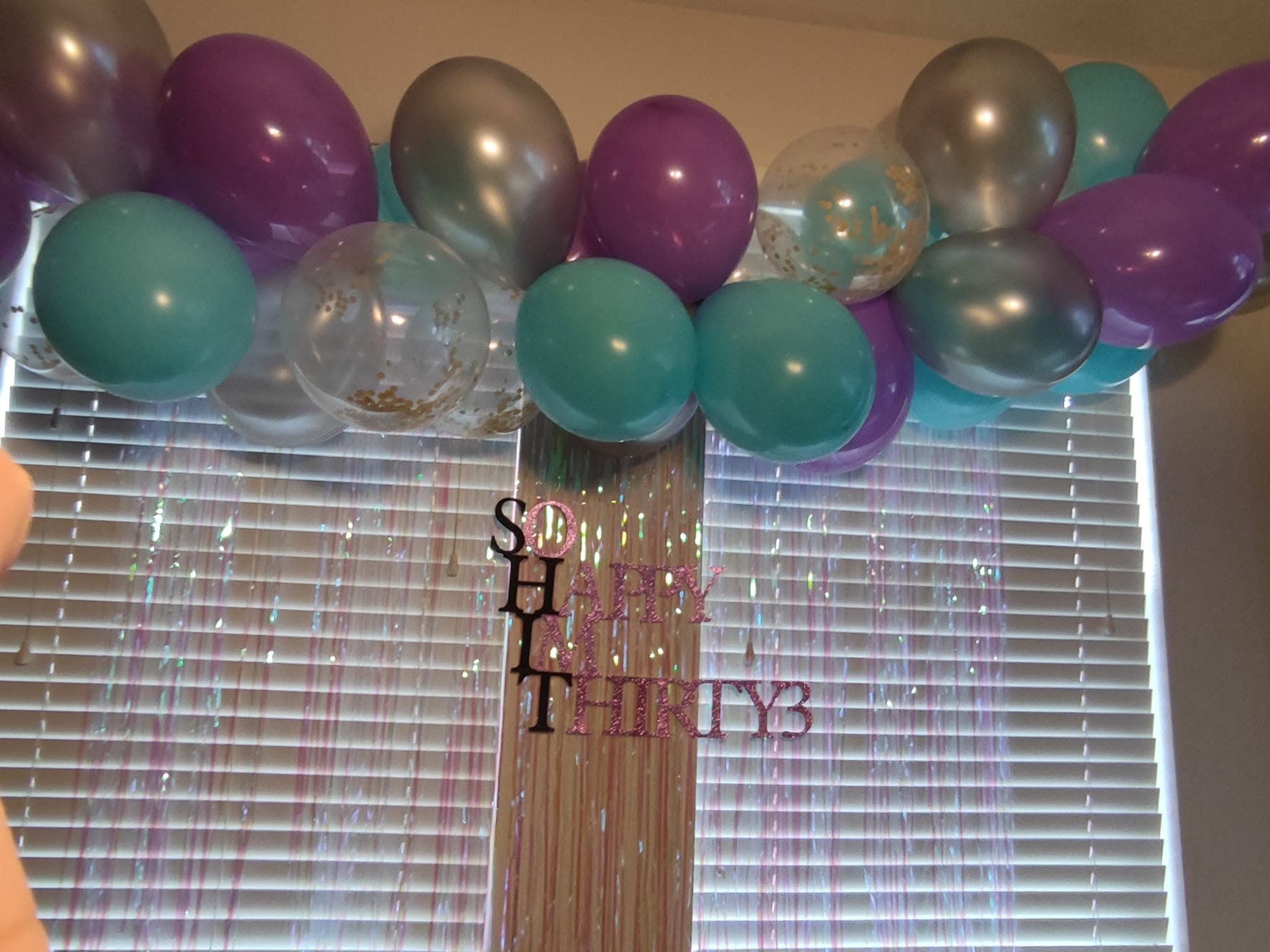 Teal, purple, silver, and confetti balloon garland with tinsel backdrop for a thirtieth birthday.