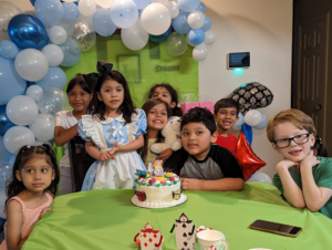 Blue and white organic balloon garland above a themed birthday party table with cake and young guests.