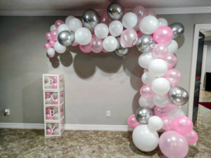 Organic pink, white, and chrome silver balloon garland draping to the floor beside baby block boxes.