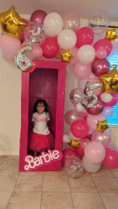 Organic pink, white, and hot-pink balloon garland with gold stars framing a doll-box photo prop for a birthday.