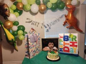 Green, white, and gold balloon garland with dinosaur foil balloons above a child's birthday cake table.