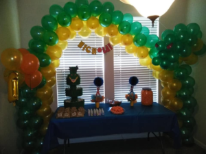Full green, yellow, and orange balloon arch in banded clusters over a themed dessert table.