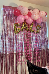 Pink and polka-dot balloon garland with gold letters on a metallic fringe backdrop for a seasonal gathering.