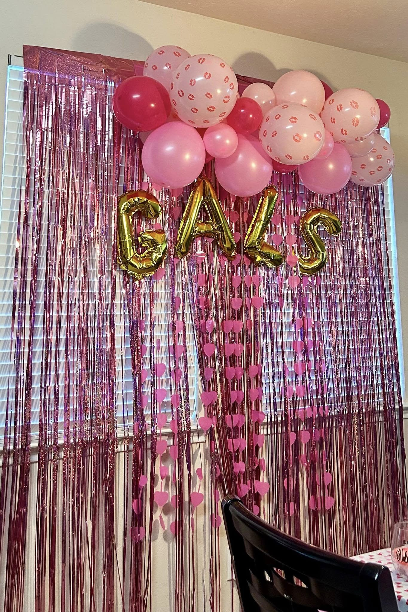 Pink and polka-dot balloon garland with gold letters on a metallic fringe backdrop for a seasonal gathering.