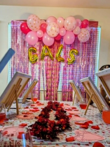 Soft pink organic garland over a fringe backdrop with gold letter balloons for a paint-party celebration.