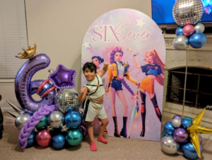 Floating balloon column with chrome, disco-ball, and star foils beside a printed birthday backdrop.