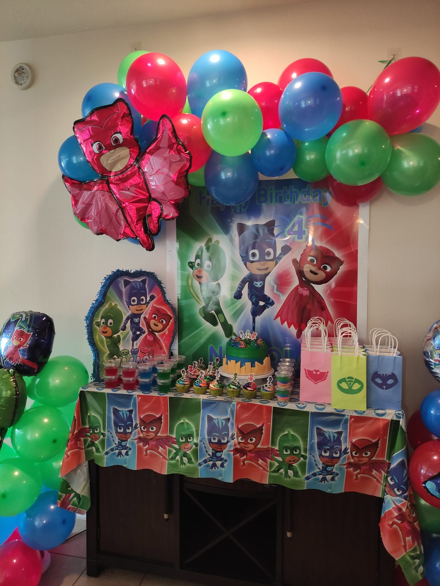 Red, blue, and green balloon garland clusters above a themed birthday dessert and favor table.