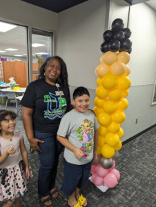 Stacked yellow, black, and pink balloon column shaped like a pencil at a school celebration.