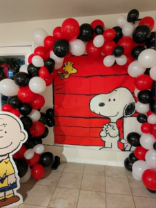 Full red, black, and white organic balloon arch framing a cartoon doghouse backdrop for a birthday.