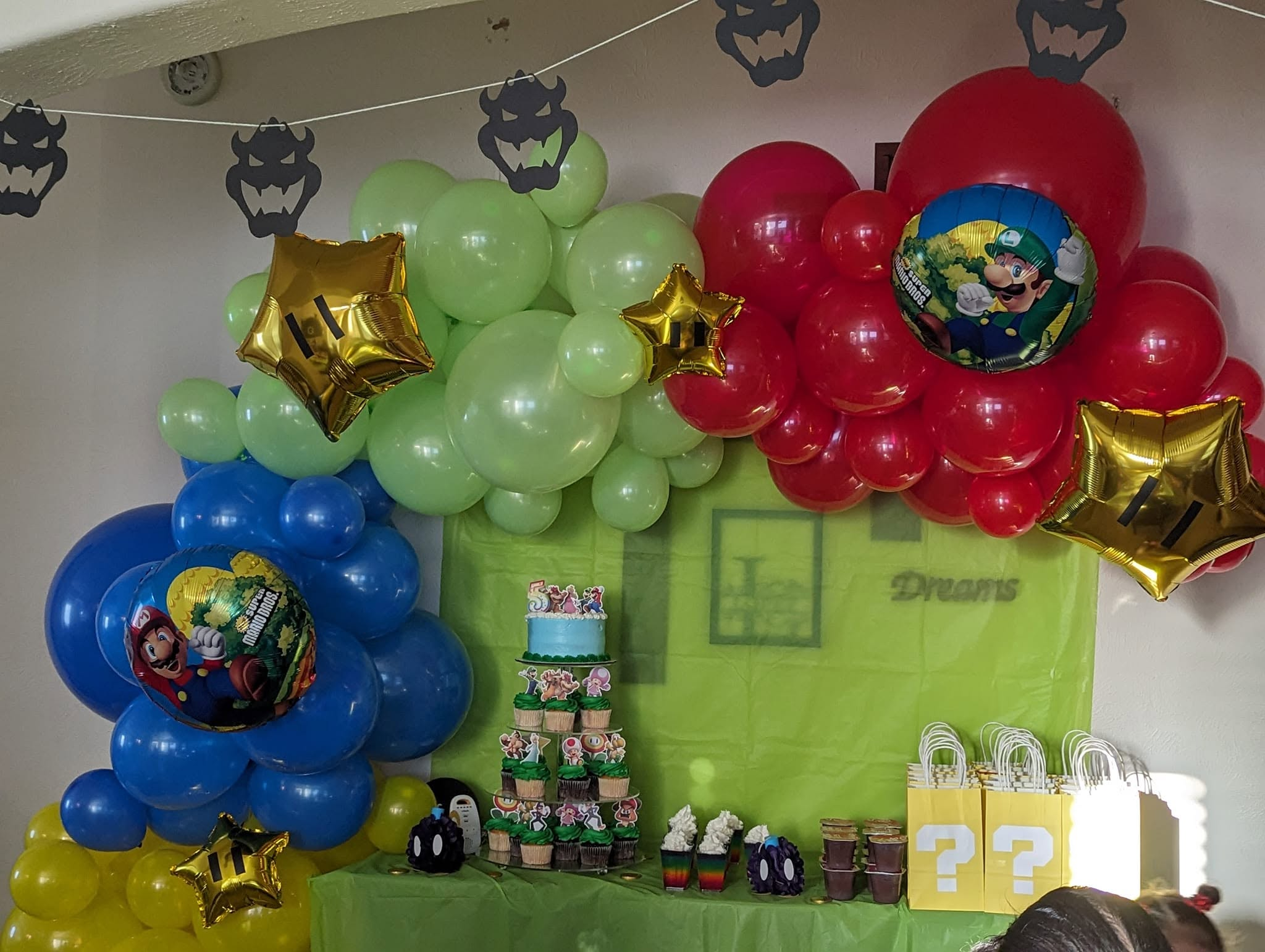 Three organic balloon clusters in blue, green, and red with gold stars above a themed dessert table.