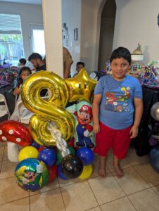 Child standing beside a gold number eight foil balloon stack at an indoor party.