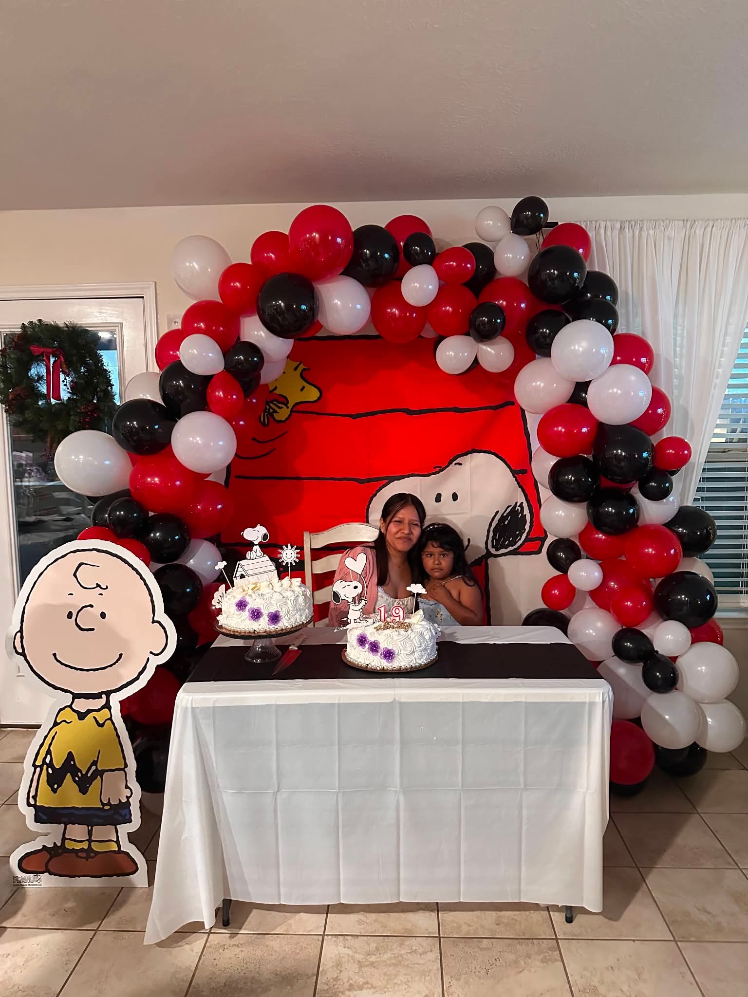 Red, black, and white organic balloon garland framing a backdrop behind a cake table.
