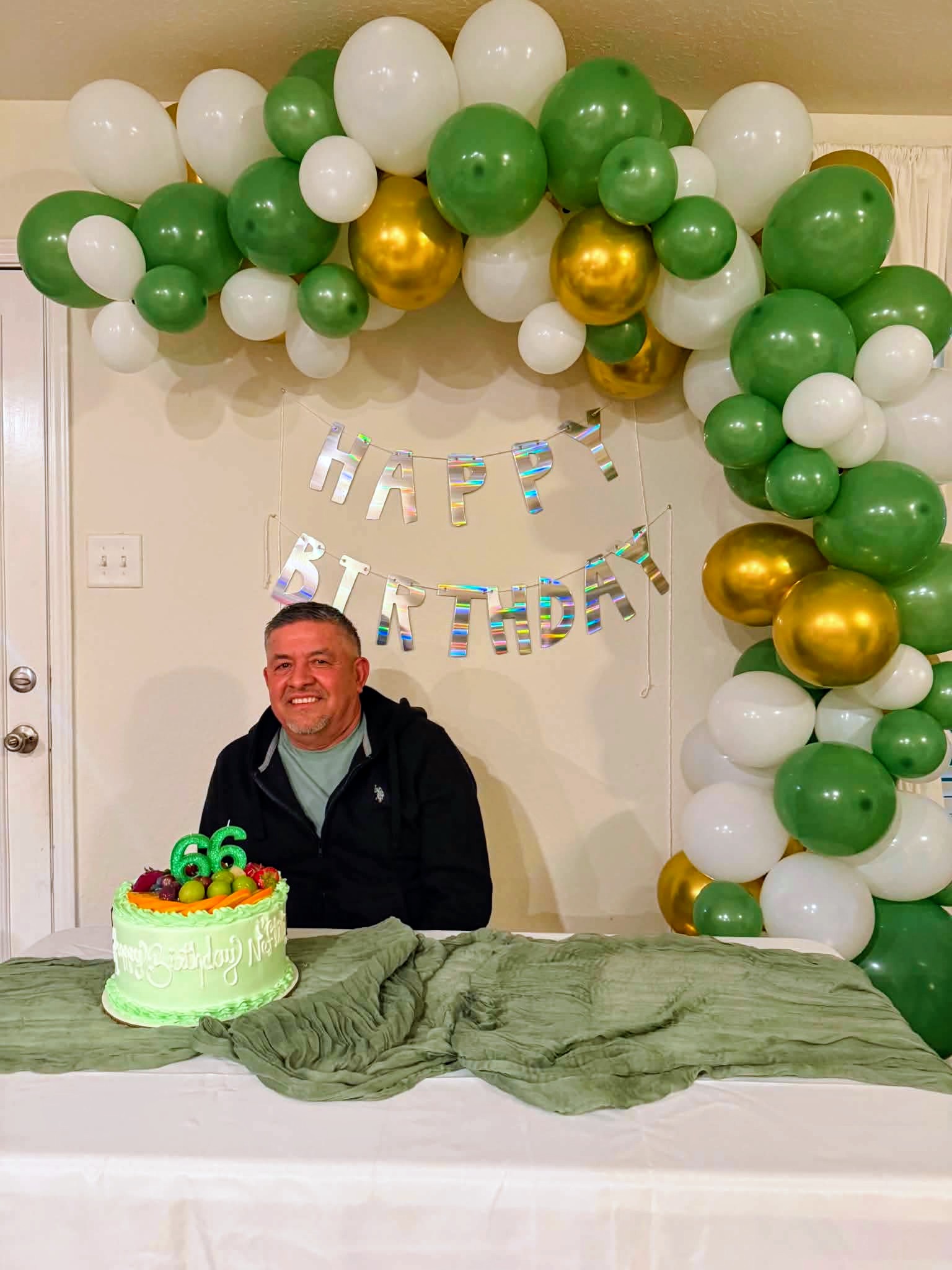 Green, white, and chrome gold organic balloon garland demi-arc above a birthday cake table.