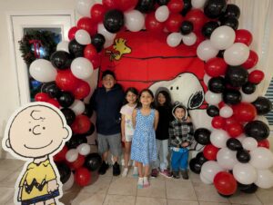 Children under a red, black, and white organic balloon arch in front of a doghouse backdrop.