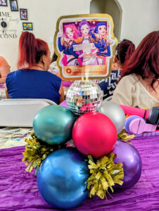 Chrome pink, blue, and teal balloon centerpiece with disco ball balloon on a purple runner.