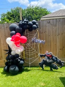 Black, red, and white balloon clusters climbing an outdoor frame with a white web accent.