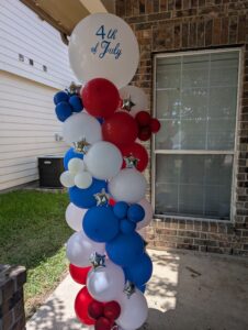Red, white, and blue balloon column with star accents and a jumbo printed topper balloon on a porch.