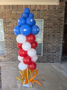 Stacked balloon column with starred blue top and red and white stripes on a brick porch.