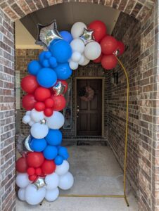Red, white, and blue organic balloon garland with silver stars dressing a gold frame at a front door.