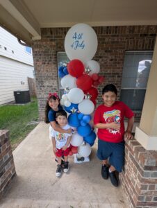 Children posing next to a red, white, and blue balloon column with a jumbo topper.