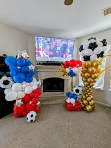 Red, white, and blue soccer-themed balloon column and gold trophy sculpture flanking a living room TV.
