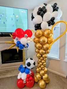 Gold trophy balloon sculpture beside a small red, white, and blue soccer ball accent piece.