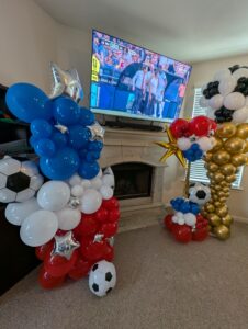 Soccer-themed balloon column and gold trophy sculpture on either side of a fireplace and TV.