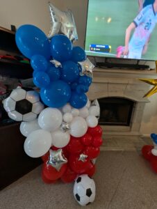 Close view of a red, white, and blue balloon column with soccer balls and silver stars.