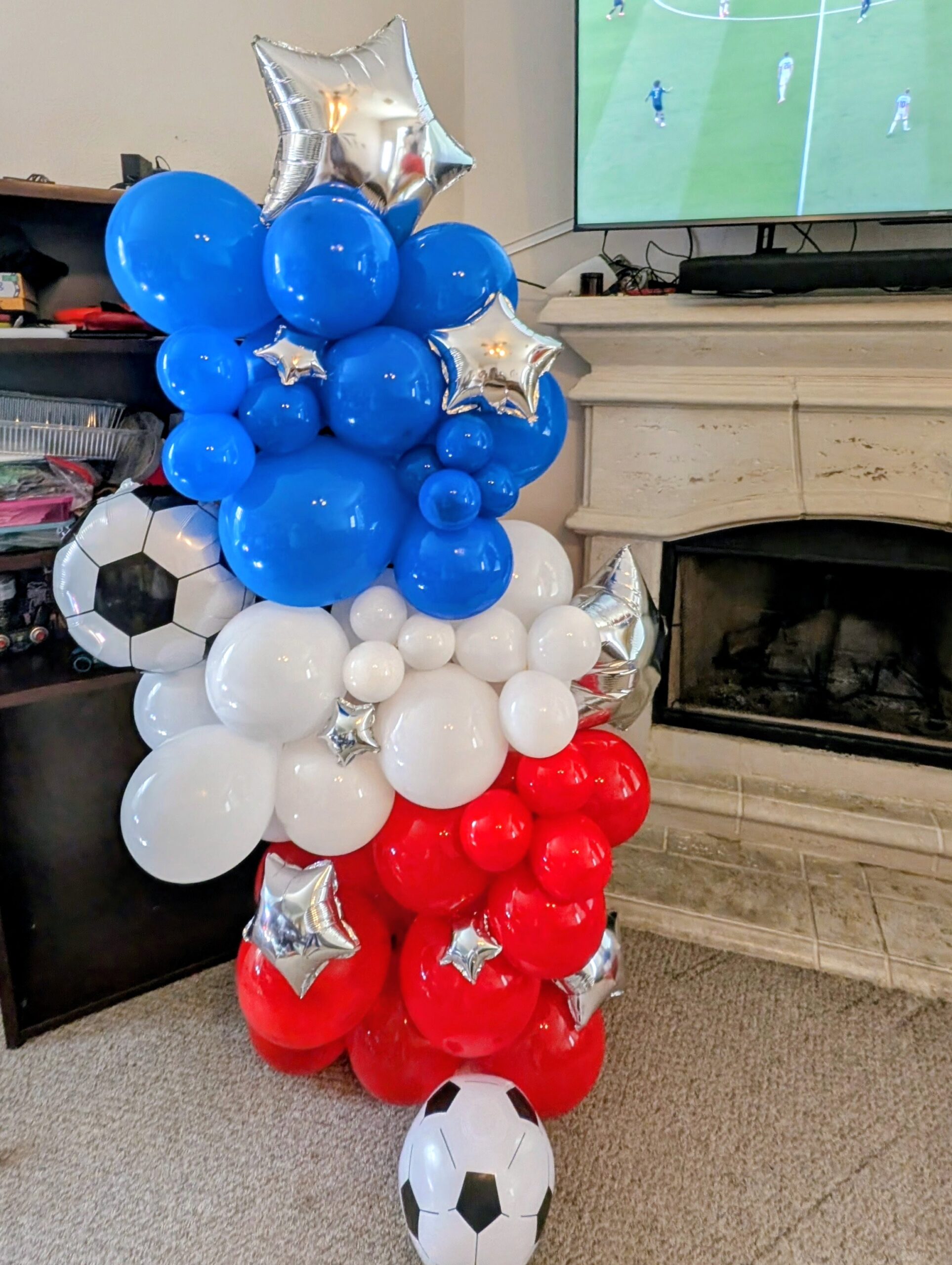 Blue, white, and red cluster balloon column with star foils and a soccer ball balloon.