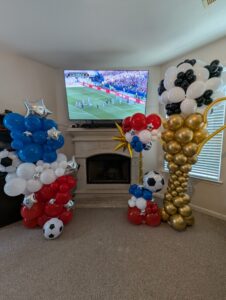 Balloon columns in team colors with soccer ball accents set up around a fireplace and television.