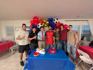 Group of guests in front of a red, blue, and gold balloon garland at a birthday party.