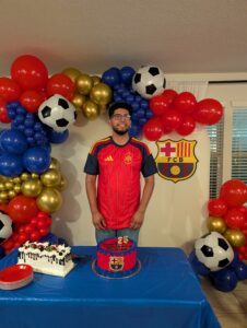 Guest of honor behind birthday cakes framed by a soccer themed organic balloon garland.