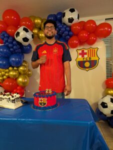 Guest of honor with a birthday cake in front of a soccer themed balloon garland.