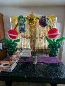 Two plant shaped balloon columns flanking a food table with gold fringe backdrop and star foil.